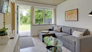 A modern living room with a grey sofa, a glass coffee table, and a view of a garden through large windows.