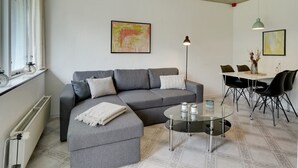 A modern living room with a grey sofa, a glass coffee table, and a dining area with a white table and black chairs.