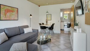 A modern living room with a grey sofa, a glass coffee table, and a dining area with a white table and black chairs.