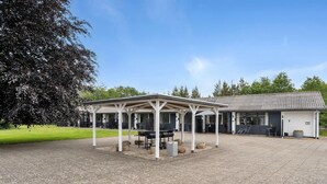 A covered outdoor seating area with tables and chairs, a building with a tiled roof, and a paved courtyard.