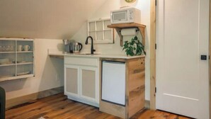 A compact kitchen with white cabinetry, a microwave on a wooden shelf, a sink, and a clock on the wall. - Cozy Sanctuary/Dwtn Franklin Studio w Priv Entry (Franklin)