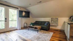 A modern living room with a wooden floor, a green sofa, a coffee table, and a TV mounted on the wall. - Cozy Sanctuary/Dwtn Franklin Studio w Priv Entry (Franklin)