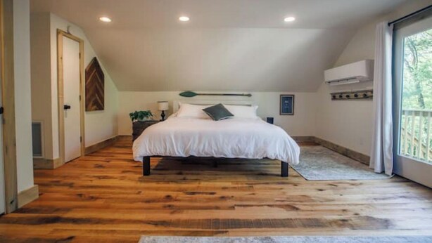 A bedroom with a wooden floor, a bed with white bedding, a nightstand with a lamp, and a window with curtains. - Cozy Sanctuary/Dwtn Franklin Studio w Priv Entry (Franklin)