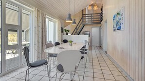 Uma cozinha moderna com ilha central, área de refeições com cadeiras e escada que leva a um andar superior.