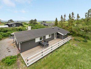 A modern house with a deck, surrounded by greenery and a clear view of the sea.