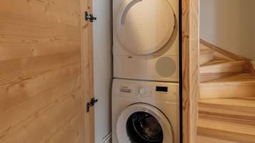 A compact laundry area with two stacked washing machines, a wooden staircase, and a wooden door.