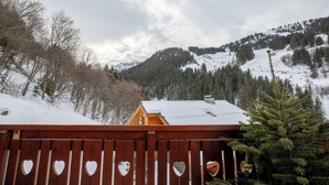 Une terrasse en bois ornée de découpes en forme de cœur, offrant une vue sur un paysage montagneux enneigé et une cabane.