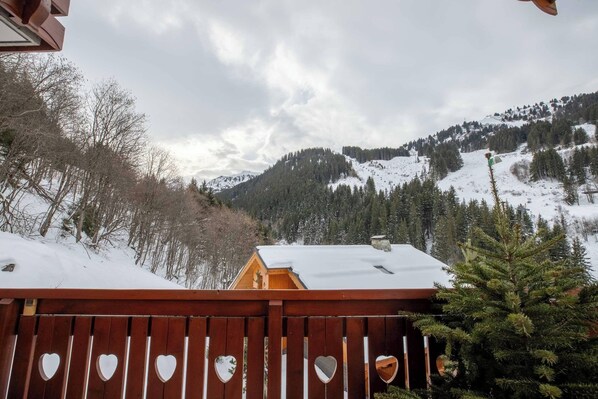 Eine Holzterrasse mit herzförmigen Ausschnitten, mit Blick auf eine verschneite Berglandschaft und eine Hütte.