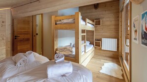 Une chambre dans un chalet en bois, avec des lits superposés, un lit avec des serviettes, un tapis blanc et une affiche accrochée au mur.