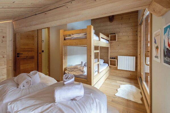 Une chambre dans un chalet en bois, avec des lits superposés, un lit avec des serviettes, un tapis blanc et une affiche accrochée au mur.