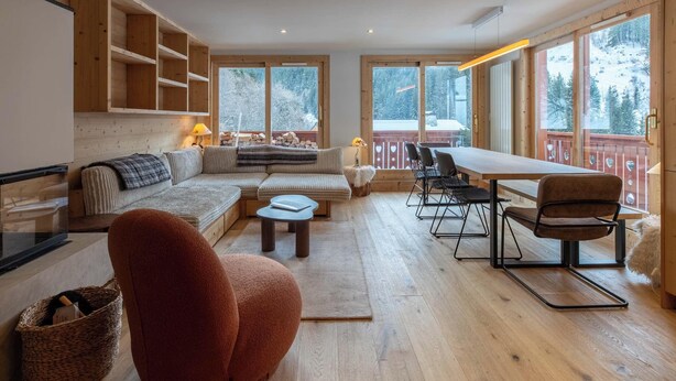 Un vaste espace de vie doté d’un plancher en bois, d’un grand canapé, d’un fauteuil rouge et d’une table à manger avec des chaises.