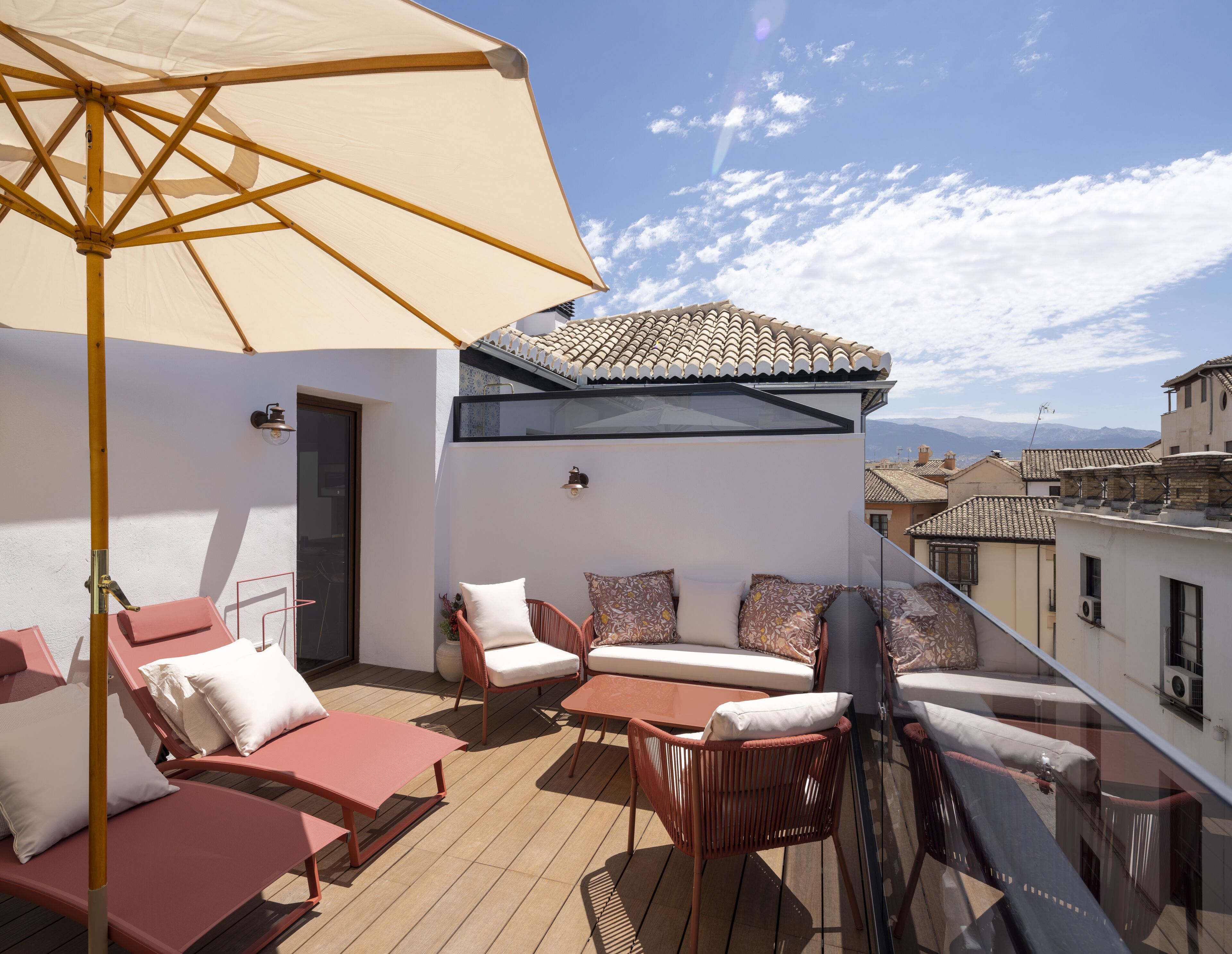 Een terras op het dak met een beige parasol, rieten meubels en een uitzicht over de stad.