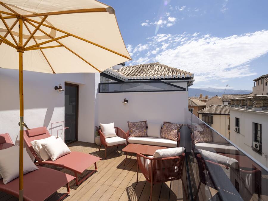 Una terraza en la azotea con una sombrilla color beige, muebles de mimbre y vistas de la ciudad.
