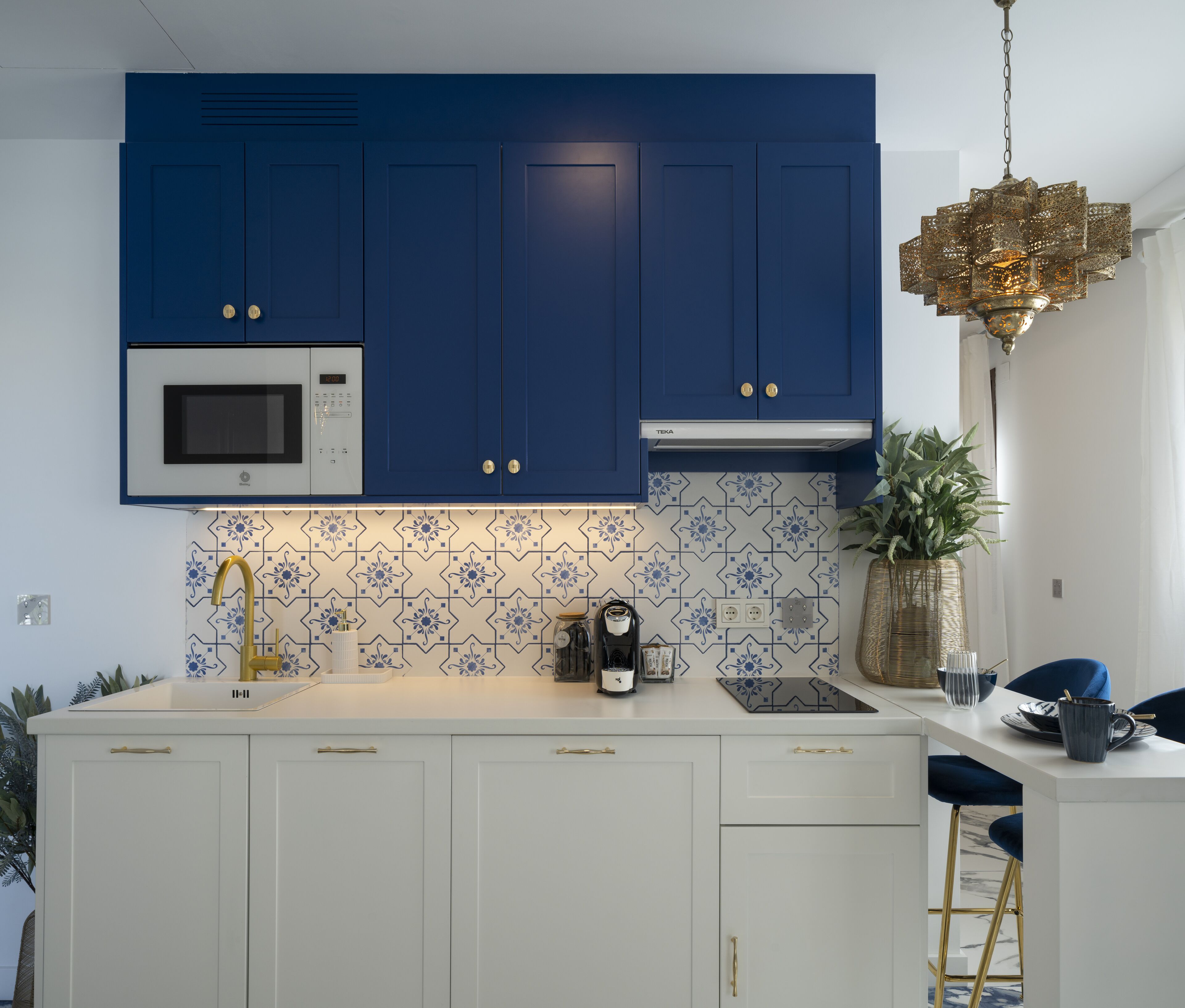 Une cuisine moderne avec des meubles bleus, des plans de travail blancs et un robinet doré.