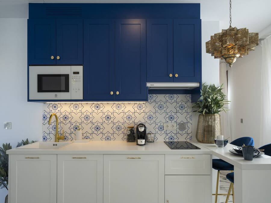 Une cuisine moderne avec des meubles bleus, des plans de travail blancs et un robinet doré.