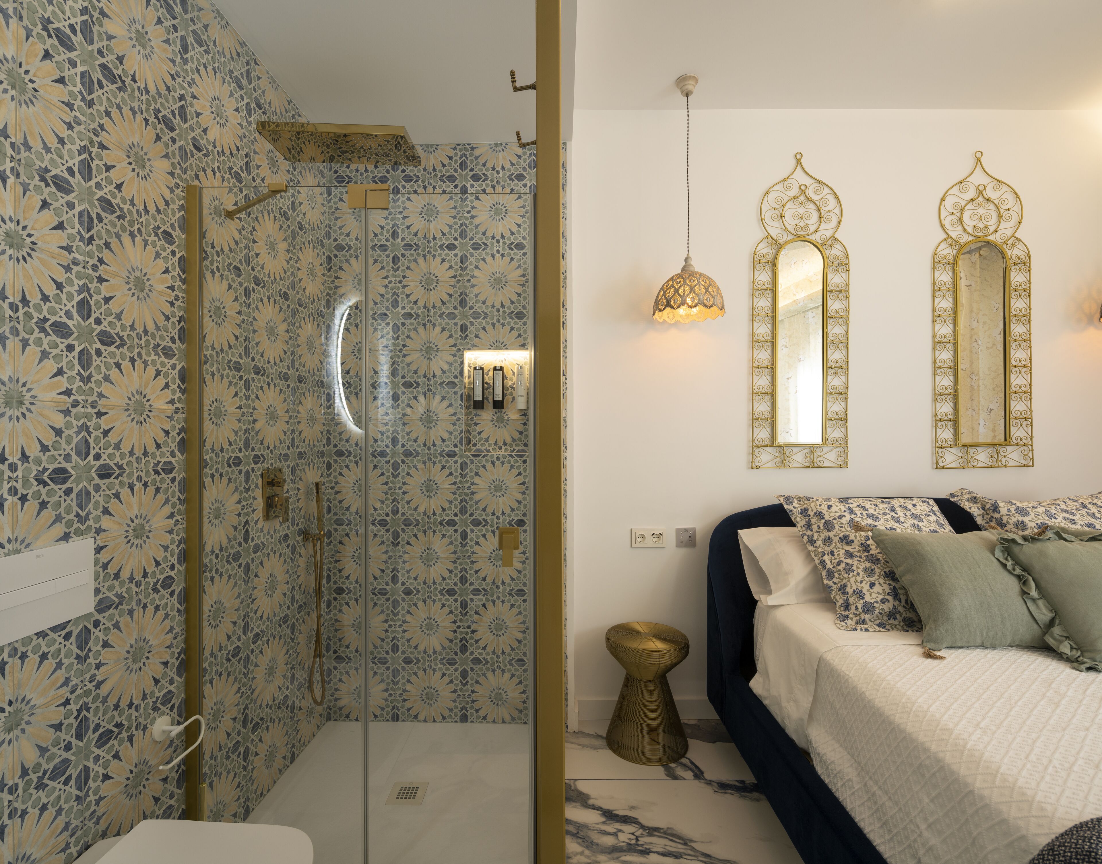 Un baño con ducha y retrete, una cama con edredón estampado, y dos espejos de pared con marcos decorativos.