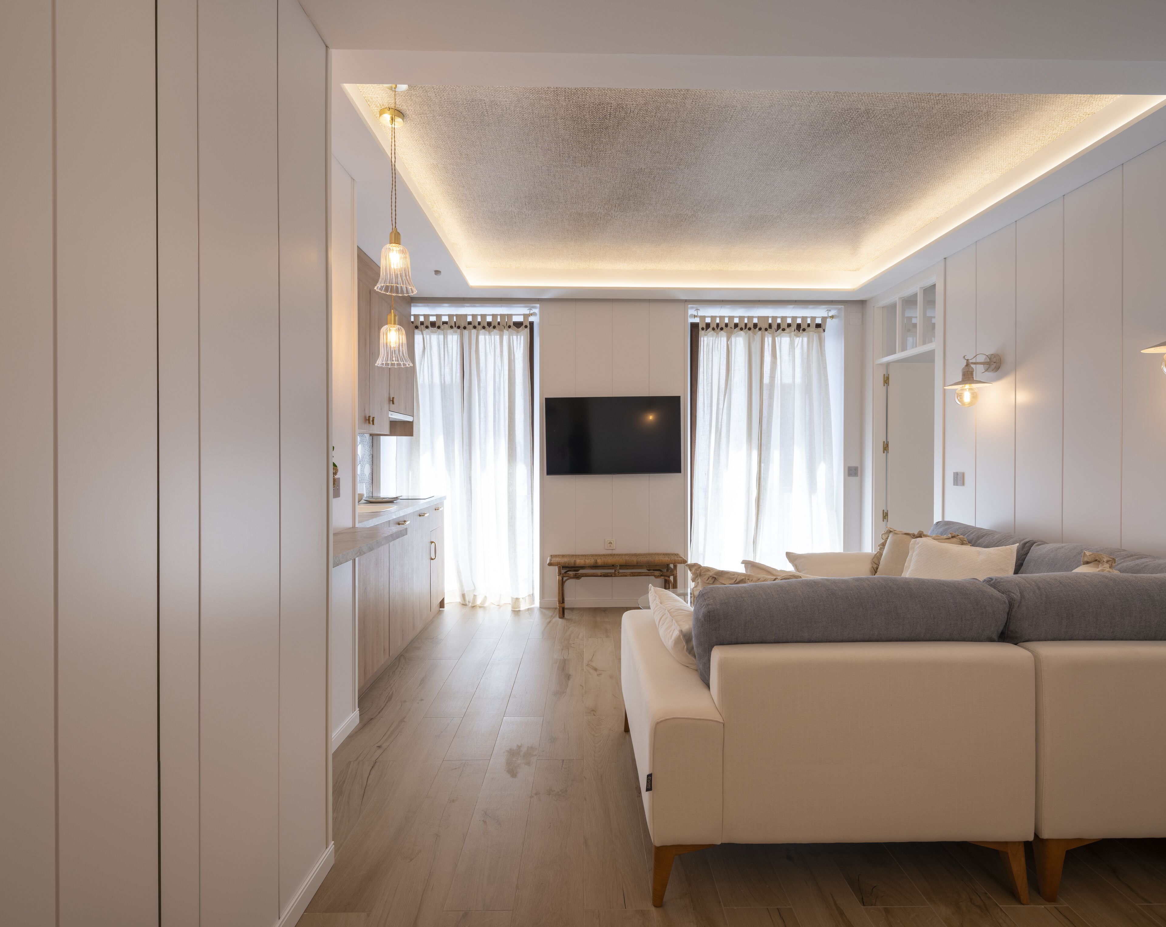 Una sala moderna con un sofá, un televisor montado en la pared y piso de madera.