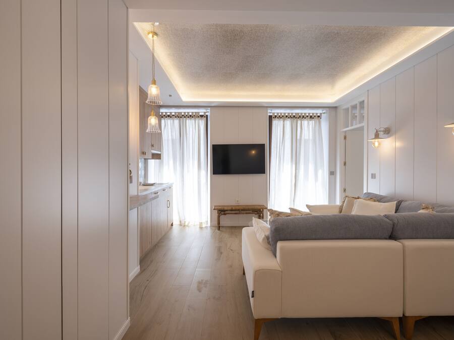 Una sala moderna con un sofá, un televisor montado en la pared y piso de madera.
