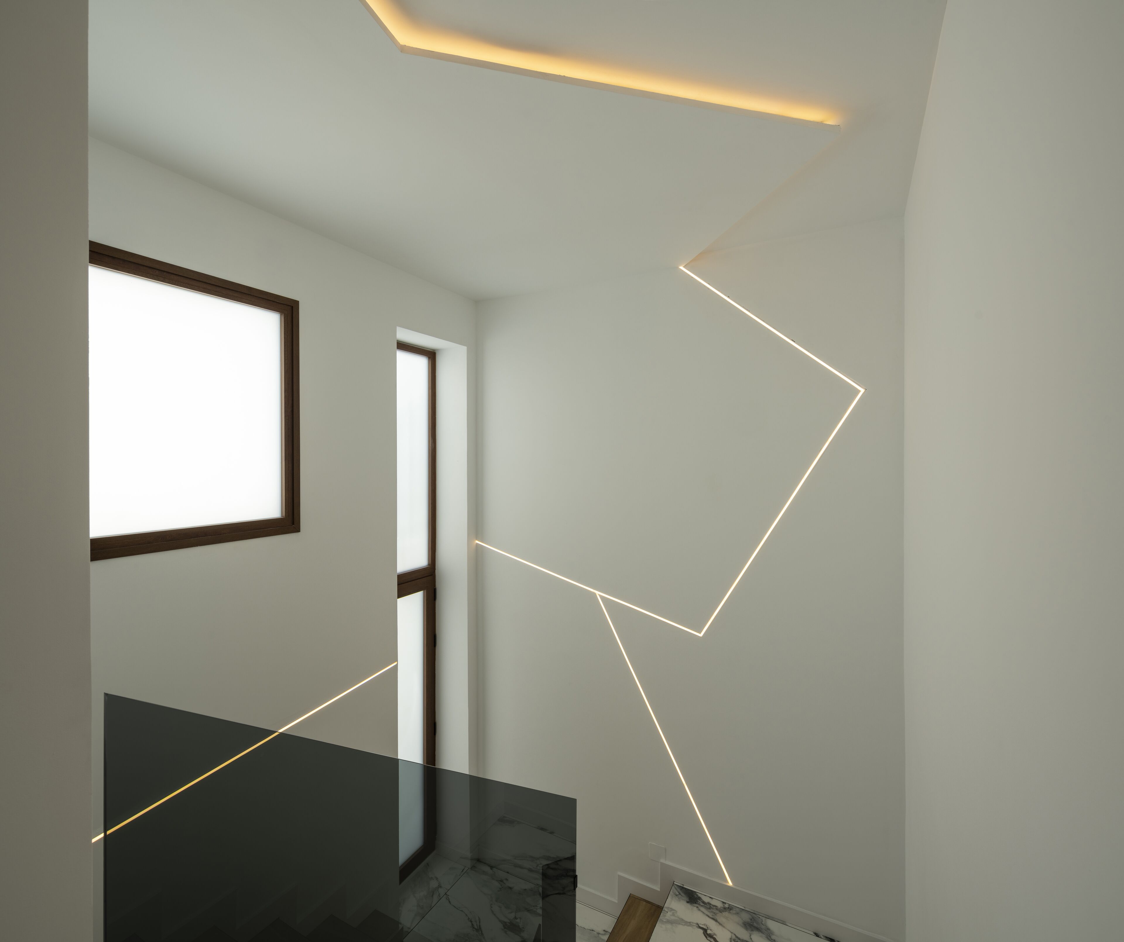 En modern inredning med en minimalistisk design, med bland annat en trappa i glas, ett stort fönster och geometriska lampor.