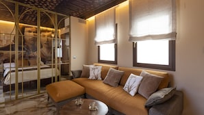 A modern living room with a sectional sofa, a round coffee table, and a glass partition with artwork. - Palatina Concept Suites (Granada)