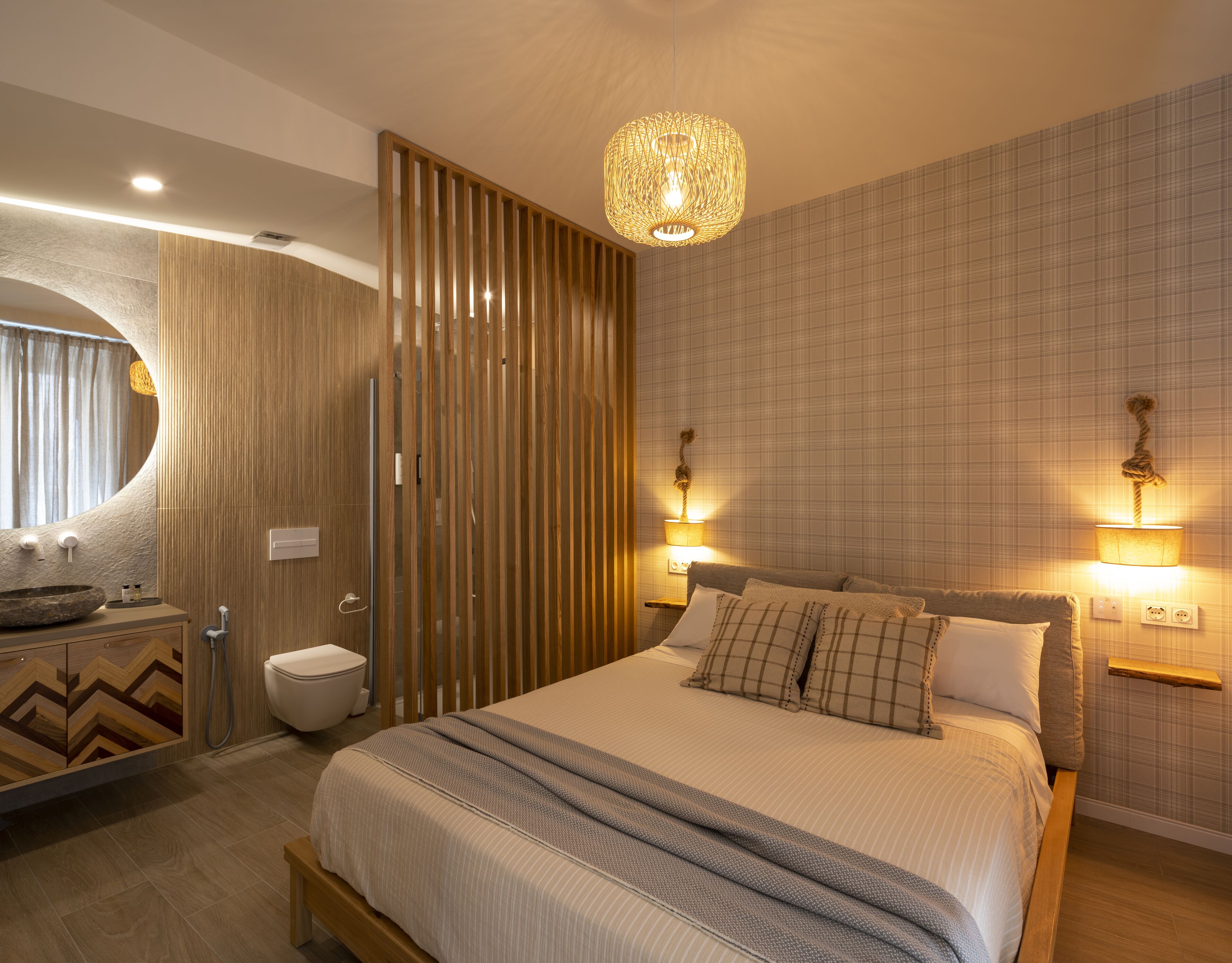 Ein modernes Schlafzimmer mit einem großen Bett, Nachttischlampen, einem Holzschrank, einem runden Spiegel und einem Badezimmer mit Waschbecken und Toilette.