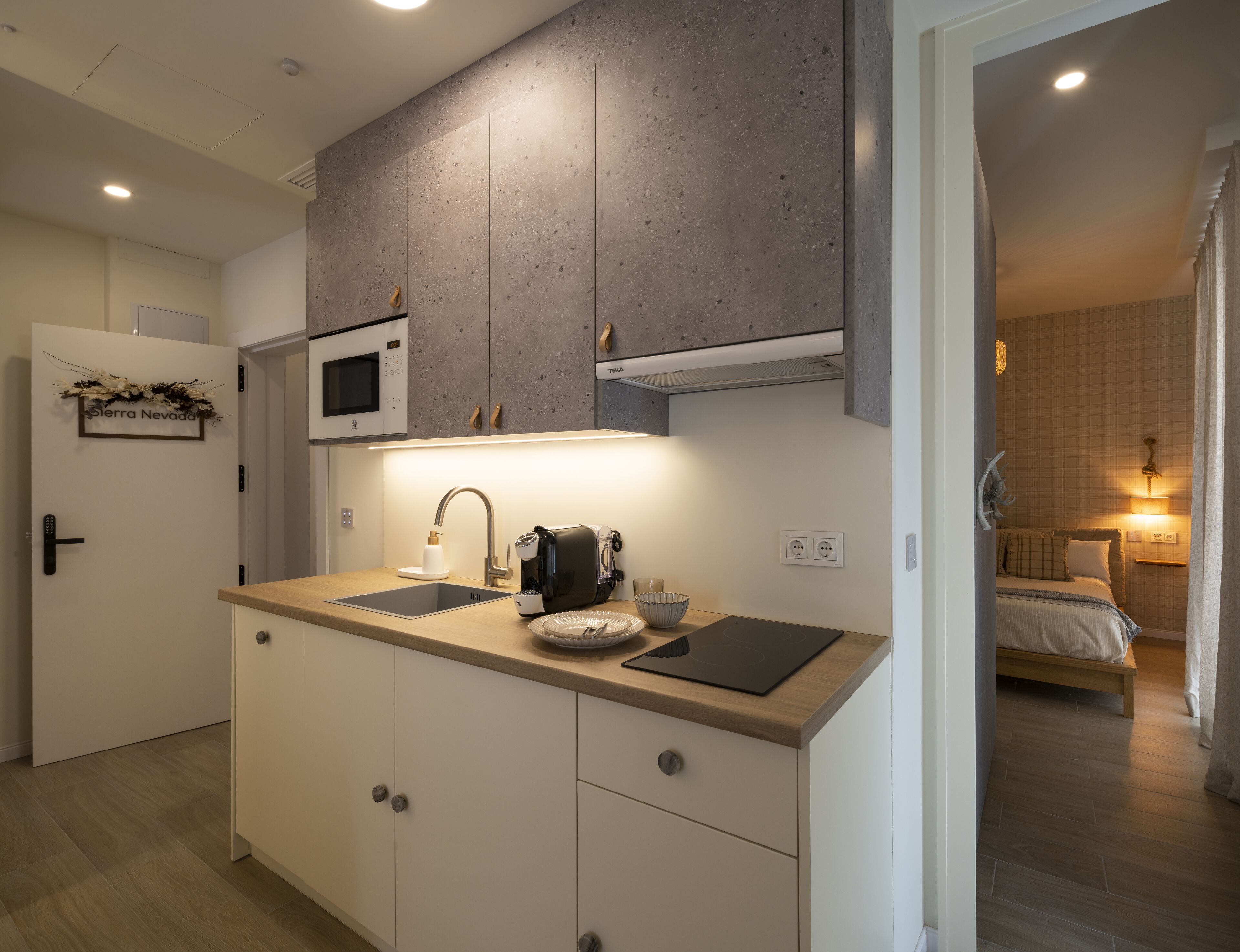 Een moderne keuken met een magnetron, een koffiezetapparaat en een gootsteen. Een bed is zichtbaar in de aangrenzende kamer.