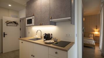 Een moderne keuken met een magnetron, een koffiezetapparaat en een gootsteen. Een bed is zichtbaar in de aangrenzende kamer.