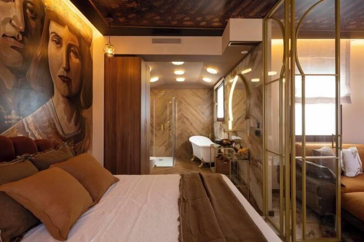 A bedroom with a large bed, a bathroom with a bathtub, and a glass-enclosed shower area.