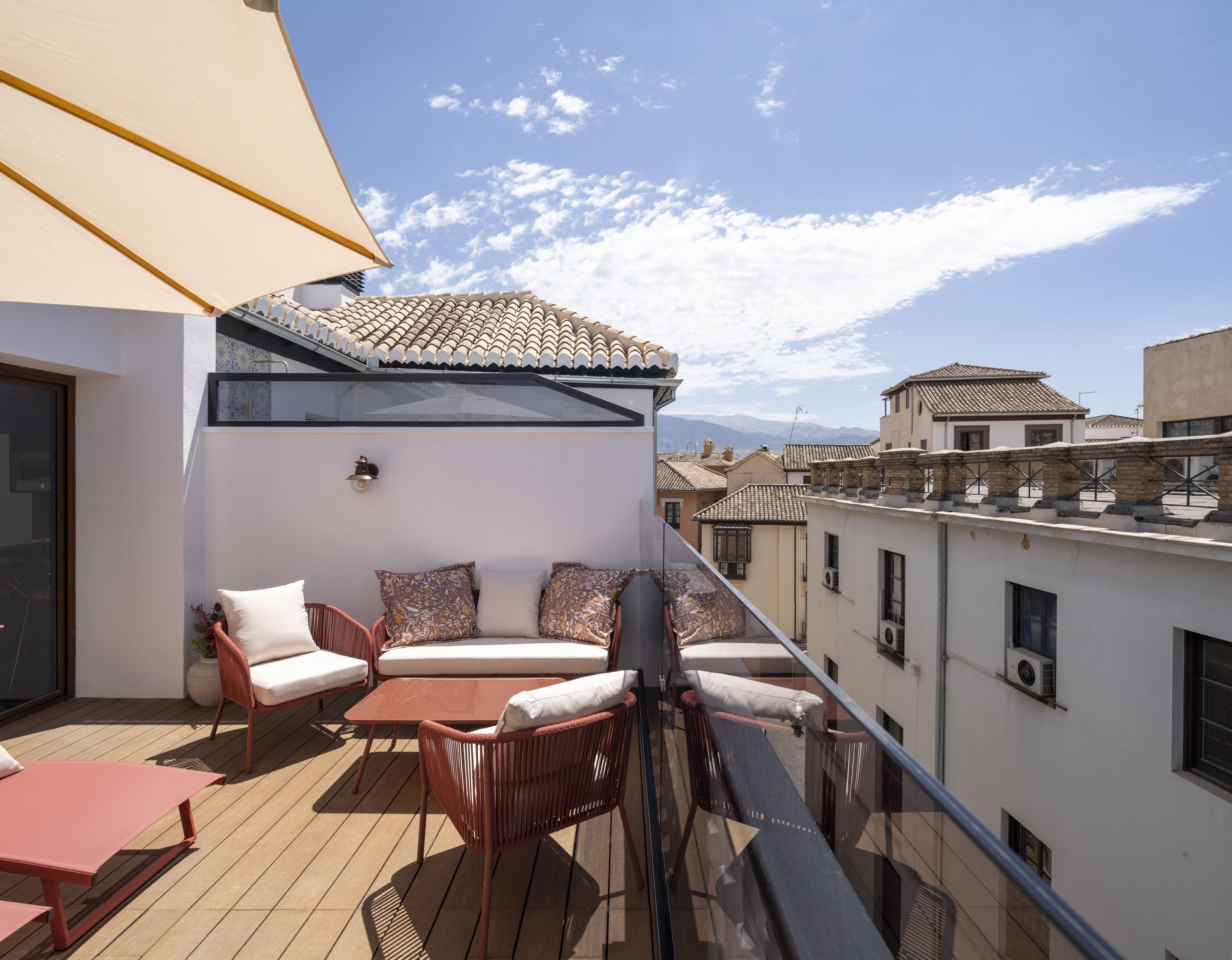 Un balcón con zona de estar, que incluye sillas y una mesa, con vistas a un paisaje urbano con edificios tradicionales.