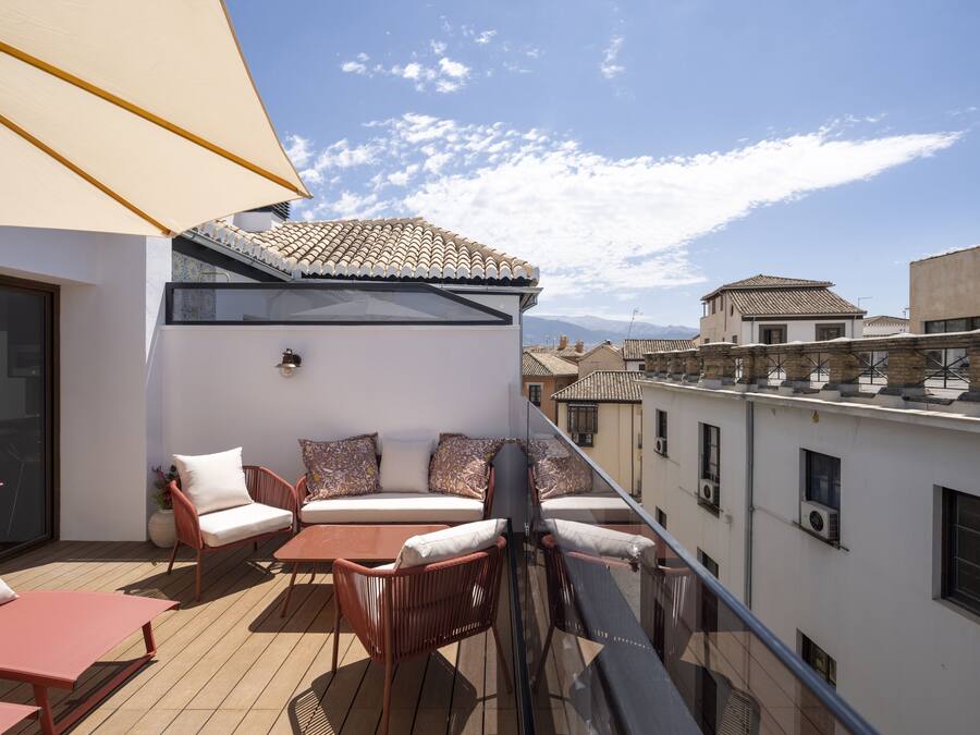 Un balcón con zona de estar, que incluye sillas y una mesa, con vistas a un paisaje urbano con edificios tradicionales.