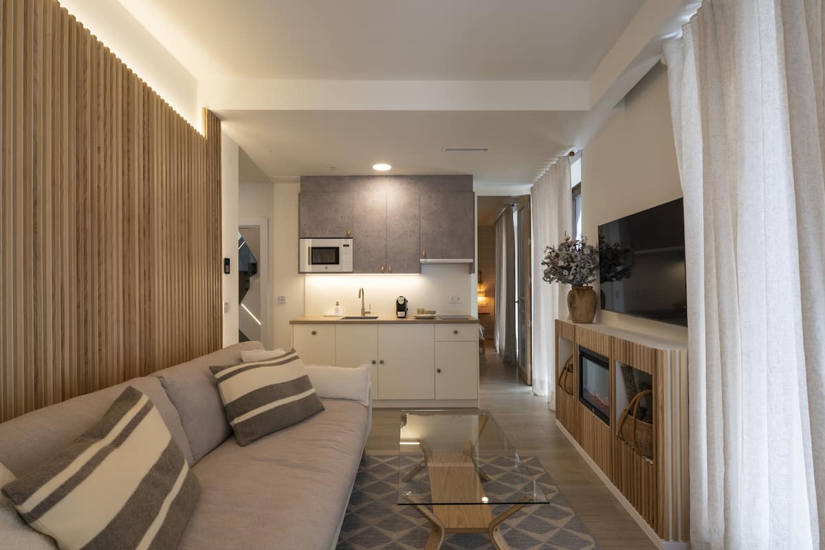 A modern living room with a sofa, a glass coffee table, and a kitchen area with a microwave and cabinets.