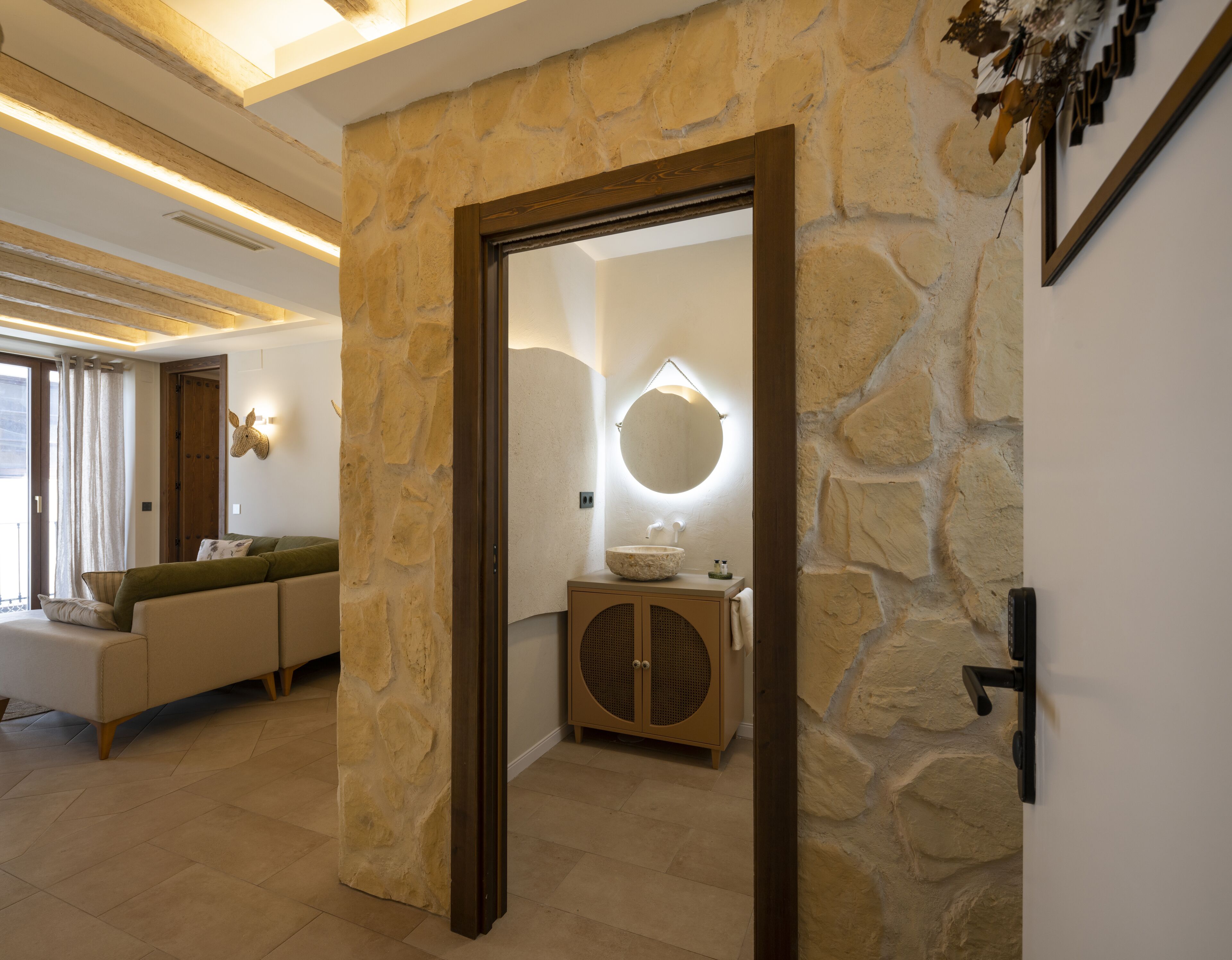 Un interior moderno con pared de piedra, puerta de madera, espejo redondo y sofá color beige.