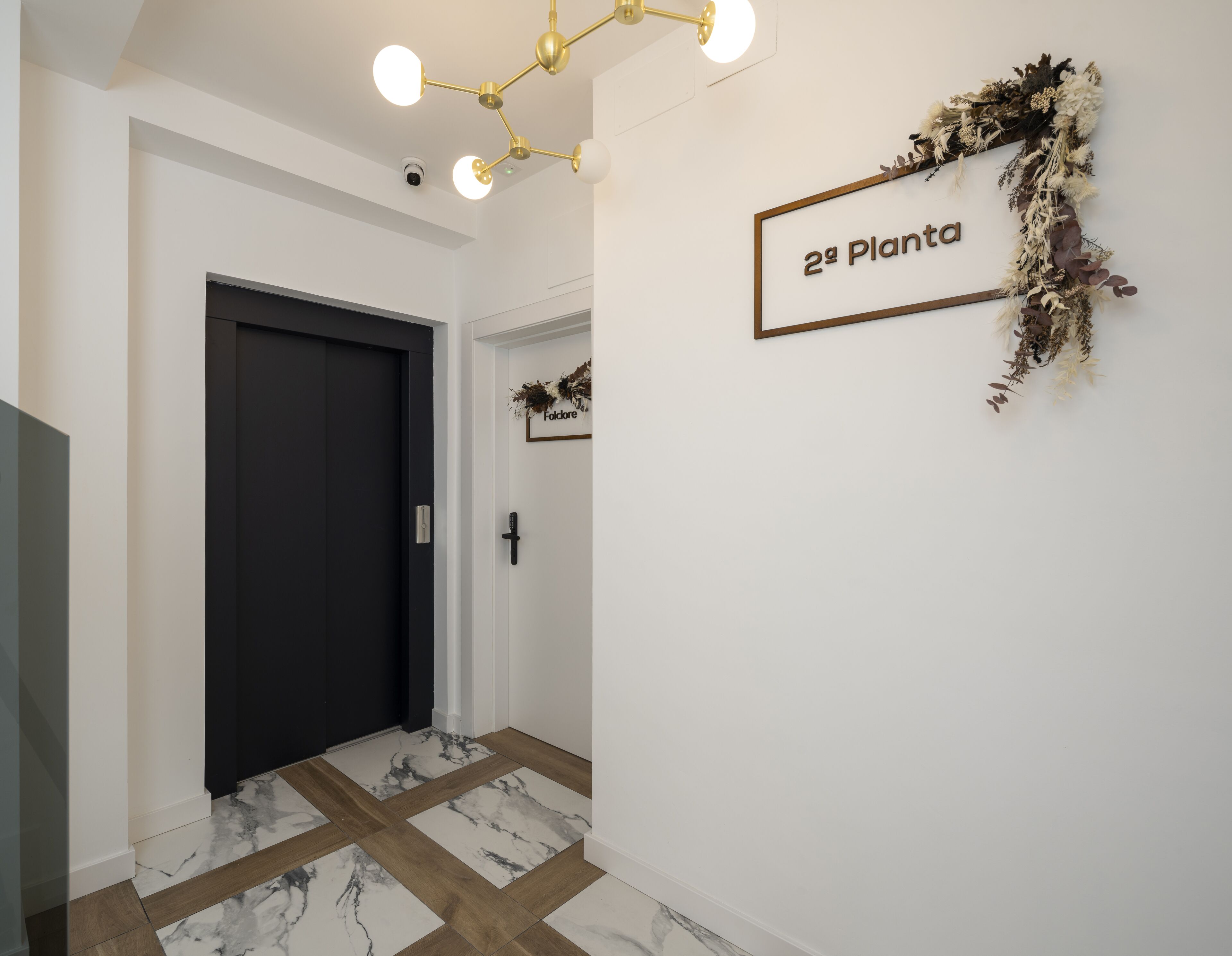 A hallway with a dark door, a wall-mounted sign reading "2ª Planta," and a decorative wreath.