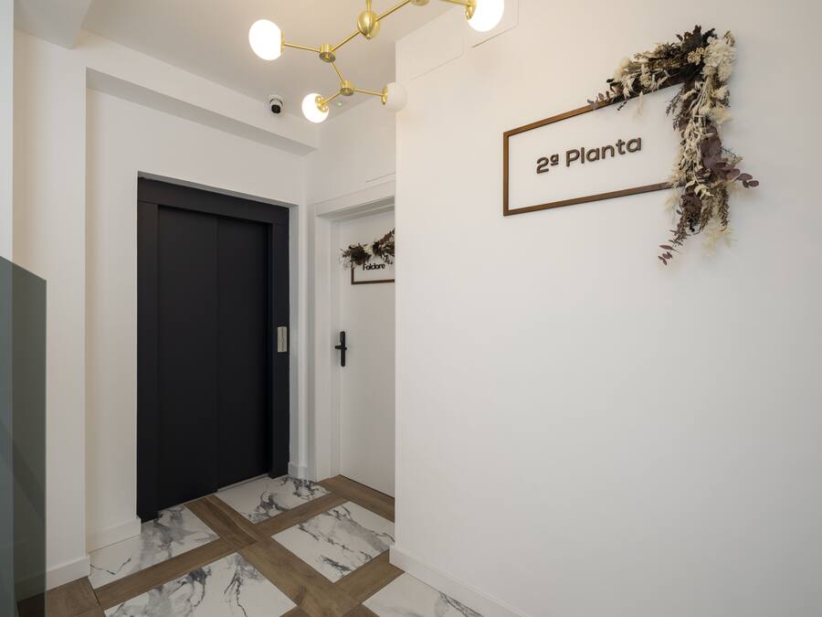 A hallway with a dark door, a wall-mounted sign reading "2ª Planta," and a decorative wreath.
