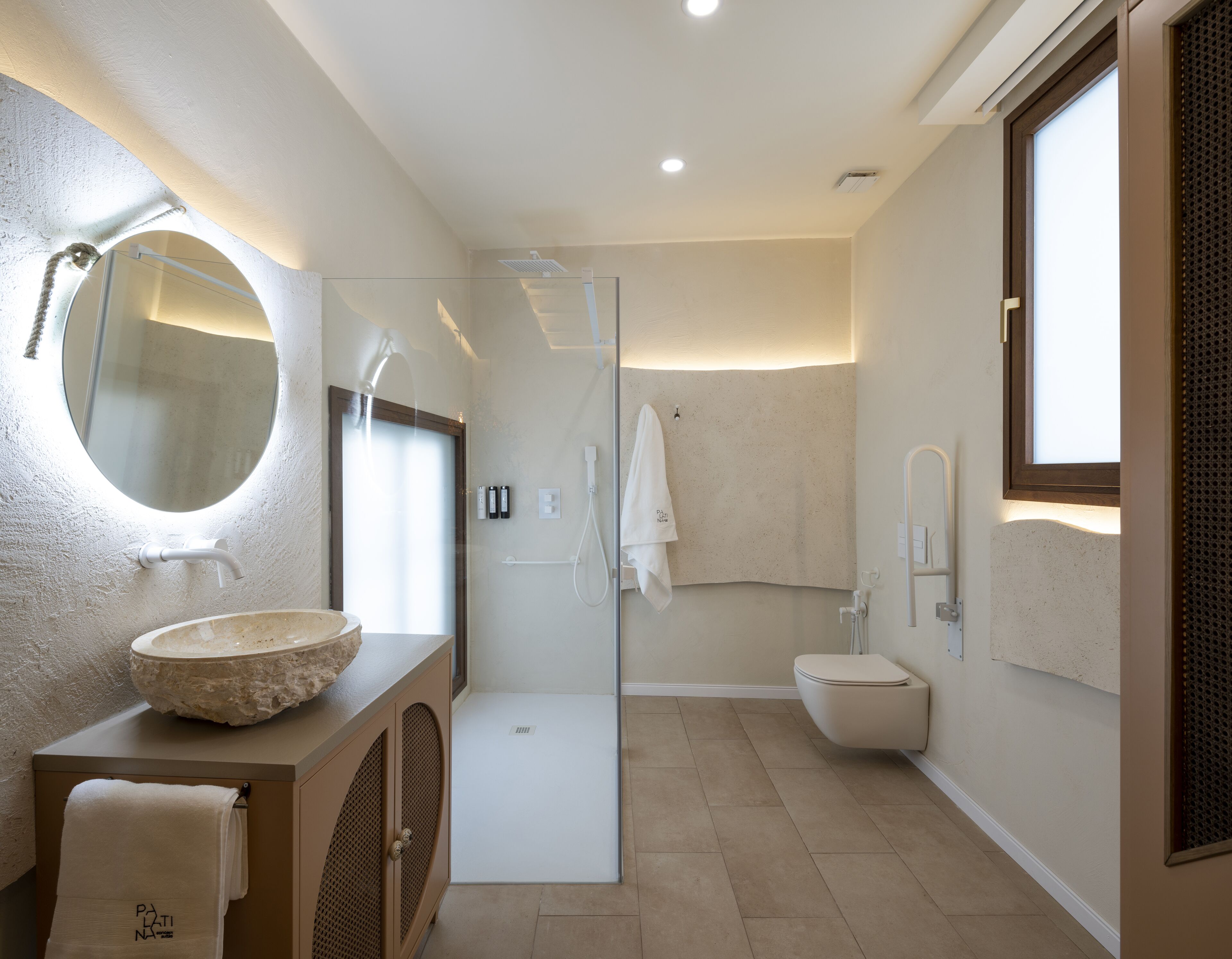 A modern bathroom with a round mirror, a stone sink, a glass-enclosed shower, and a toilet.