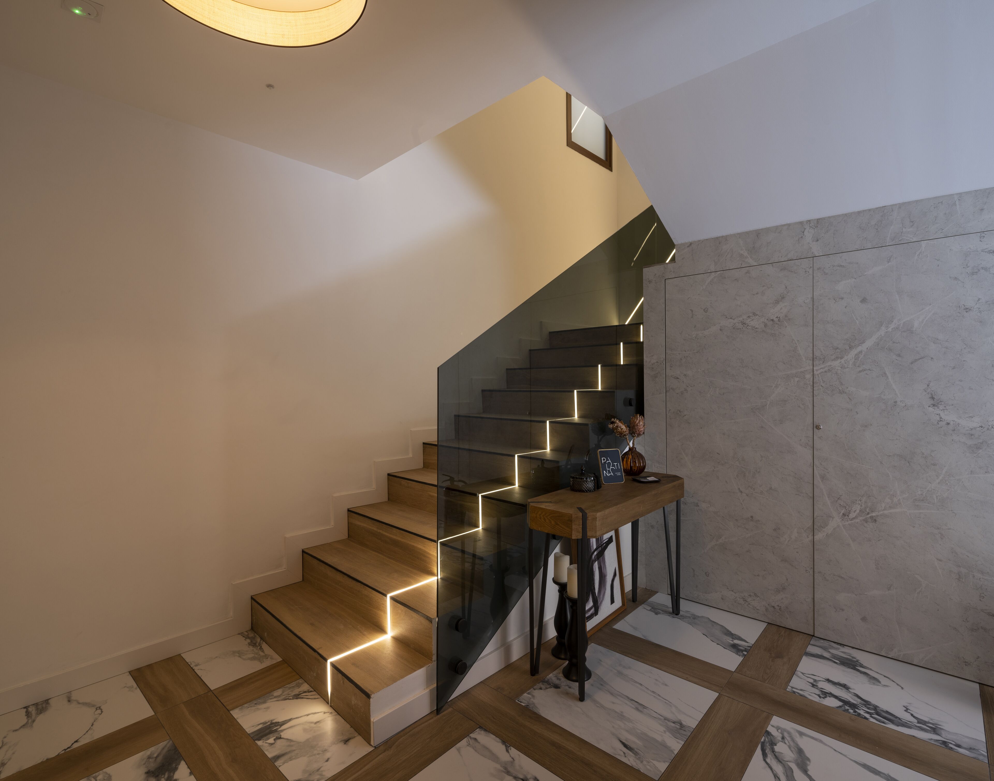 A modern staircase with glass railings and wooden steps, leading to a landing with a small table and decorative items.
