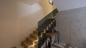 A modern staircase with glass railings and wooden steps, leading to a landing with a small table and decorative items.