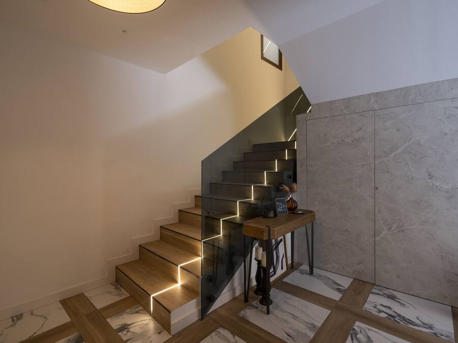 Eine moderne Treppe mit Glastrennläufen und Holzdielen, die zu einer Zwischenebene mit einem kleinen Tisch und Dekorationselementen führt.