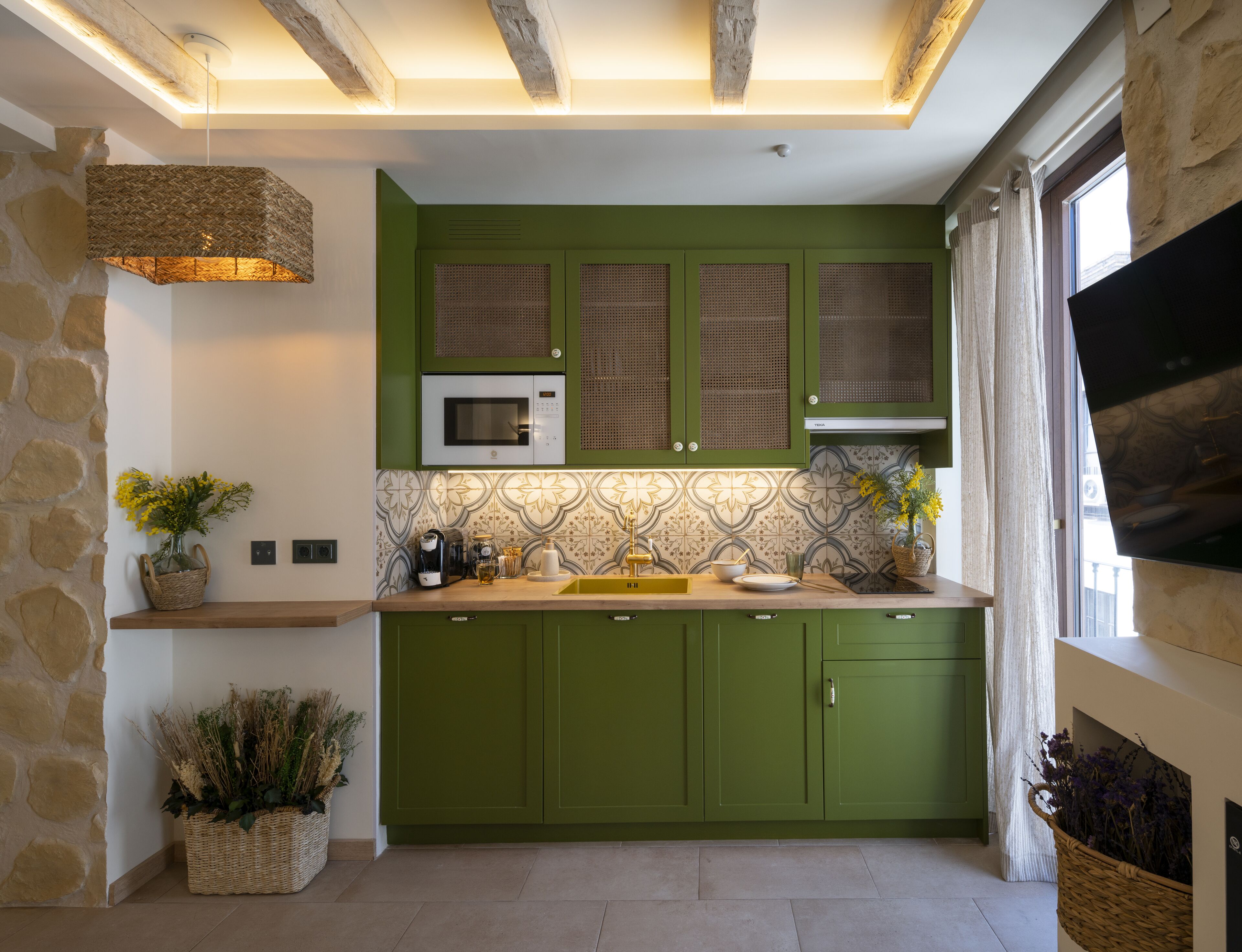 A modern kitchen with green cabinets, a microwave, and a hanging light fixture.