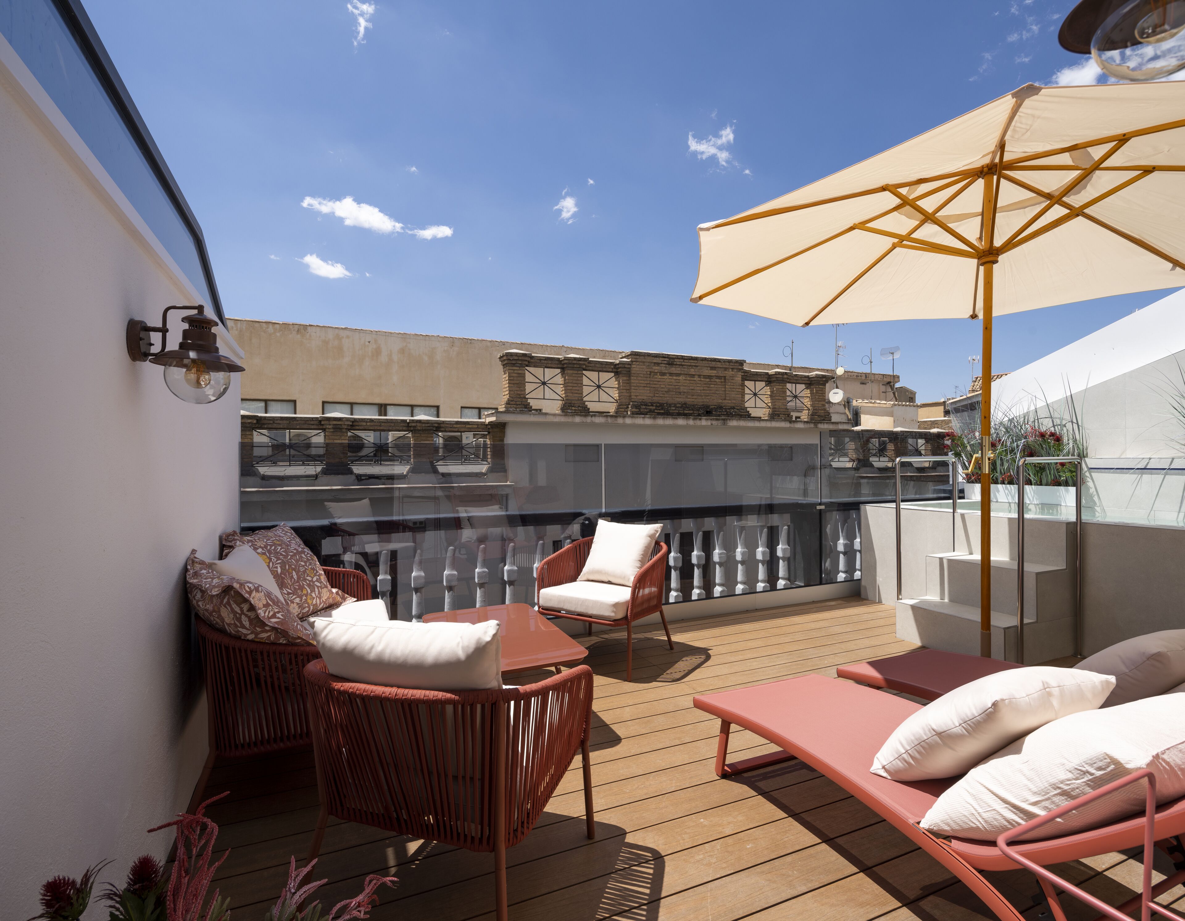 A rooftop terrace with wicker furniture, a glass balustrade, and a large umbrella.