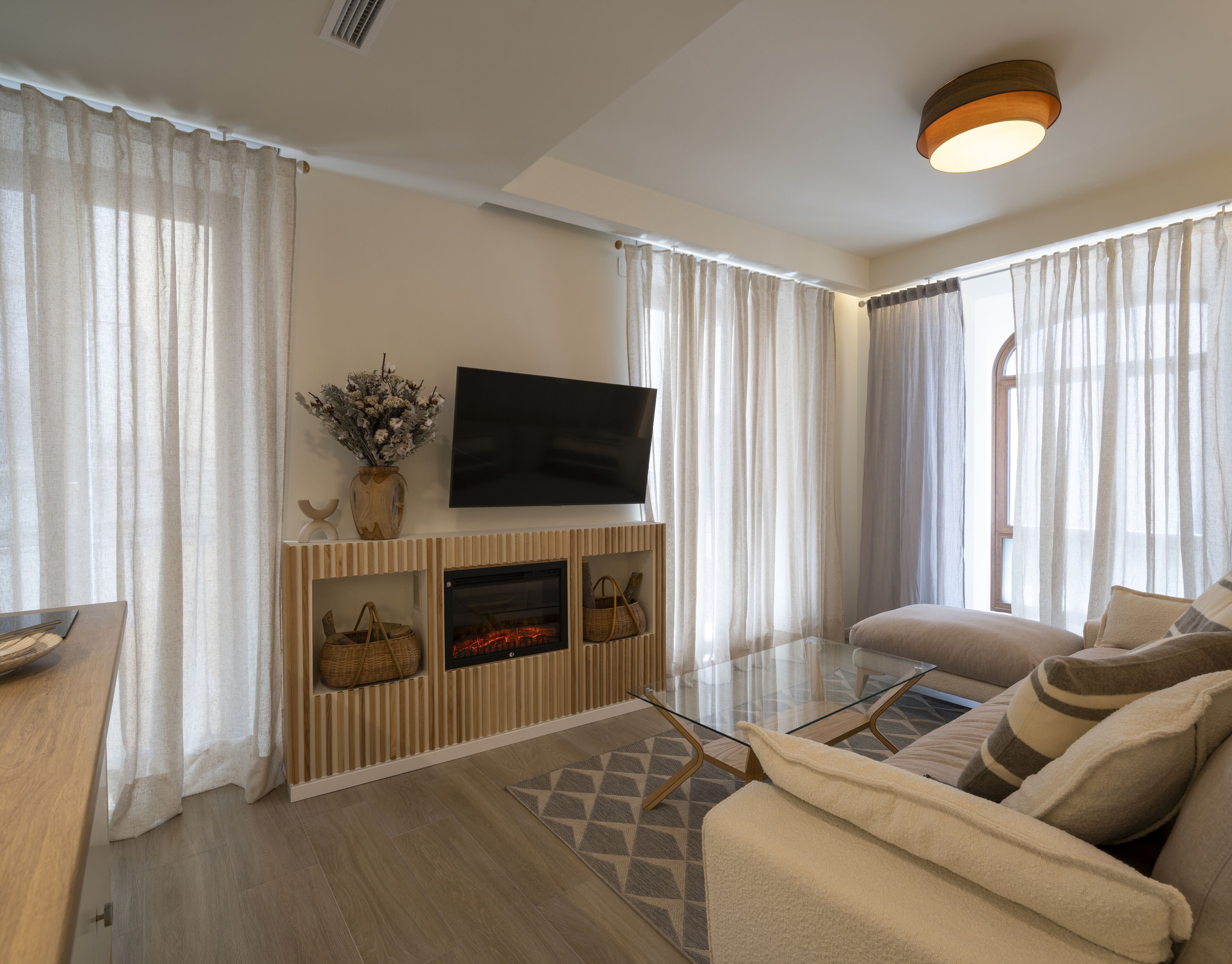 A modern living room with a flat-screen TV, wooden shelves, a fireplace, and a sofa.