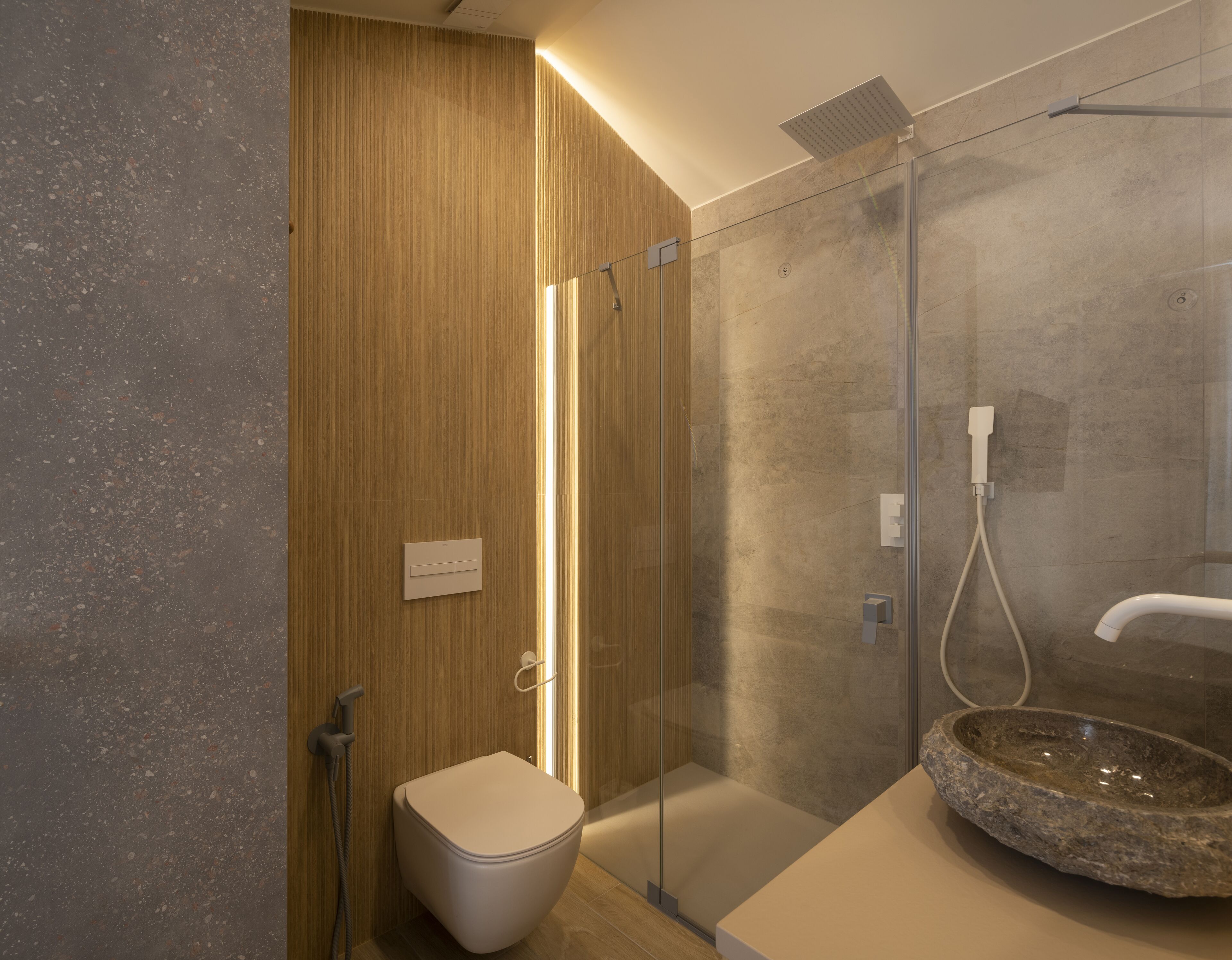 A modern bathroom with a glass-enclosed shower, a wooden vanity, and a stone basin.