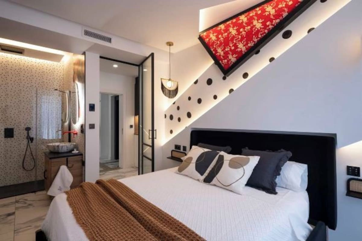 A modern bedroom with a large bed, a mirror, and a red accent wall.