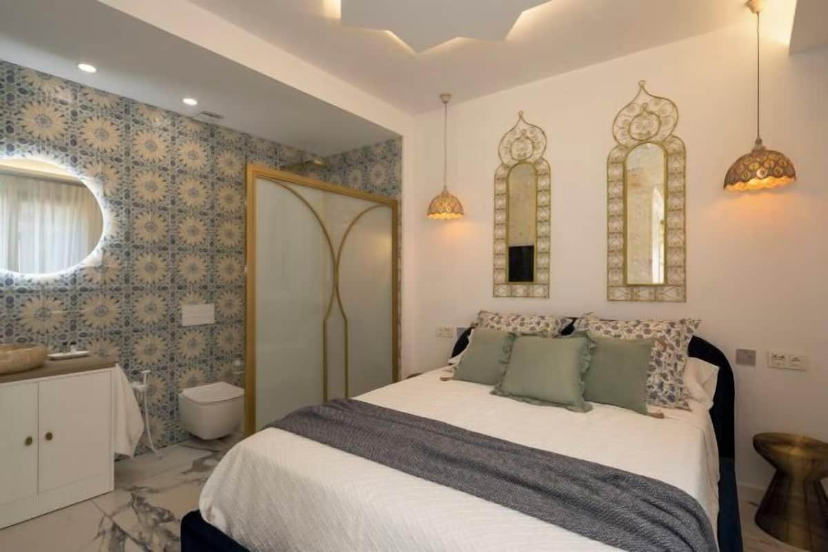 A bedroom with a bed, bedside lamps, a mirror, a wardrobe, and a bathroom.