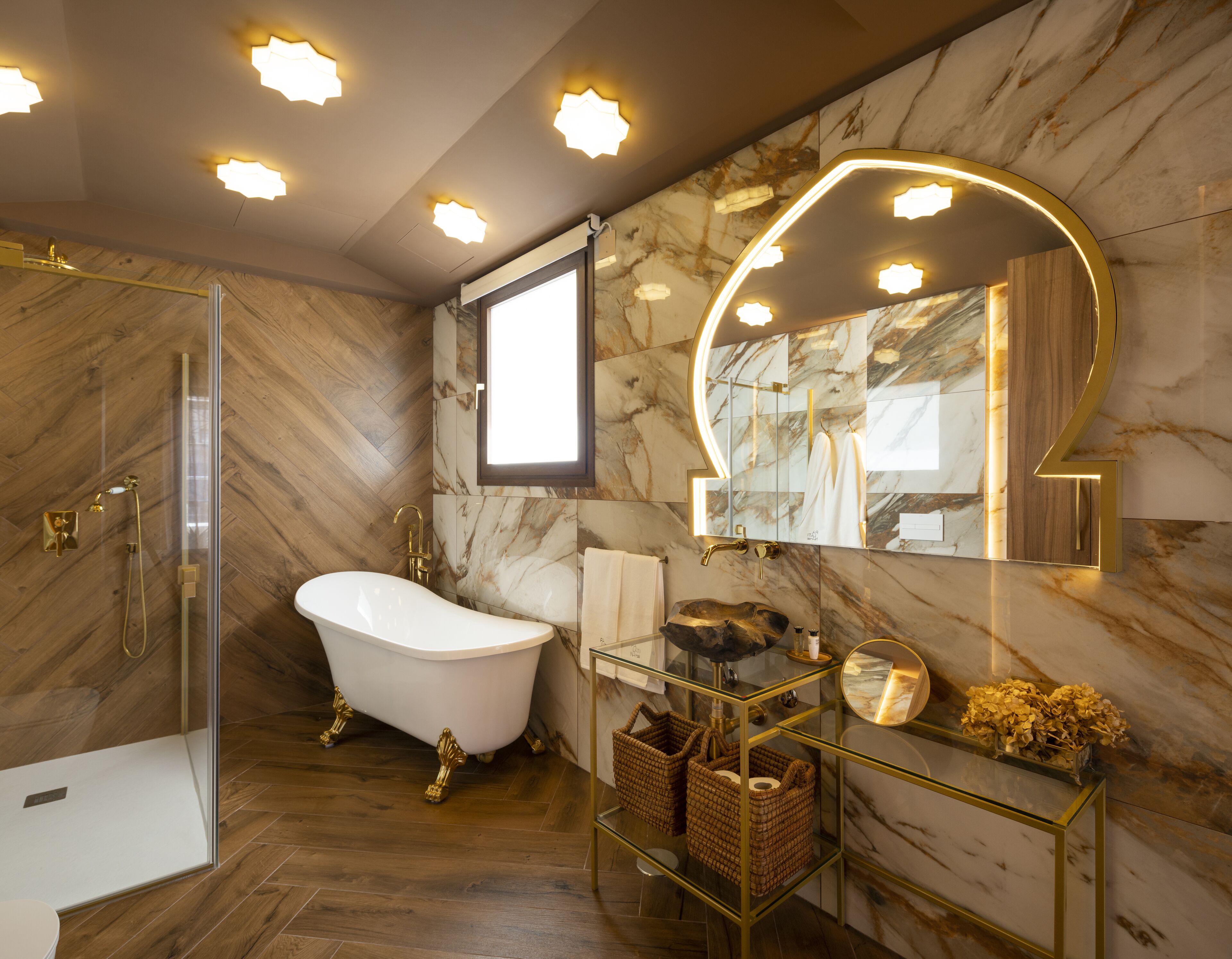 Une salle de bain dotée d’une baignoire sur pieds, d’une douche à parois de verre, de murs en marbre et d’un meuble-lavabo avec un cadre doré.