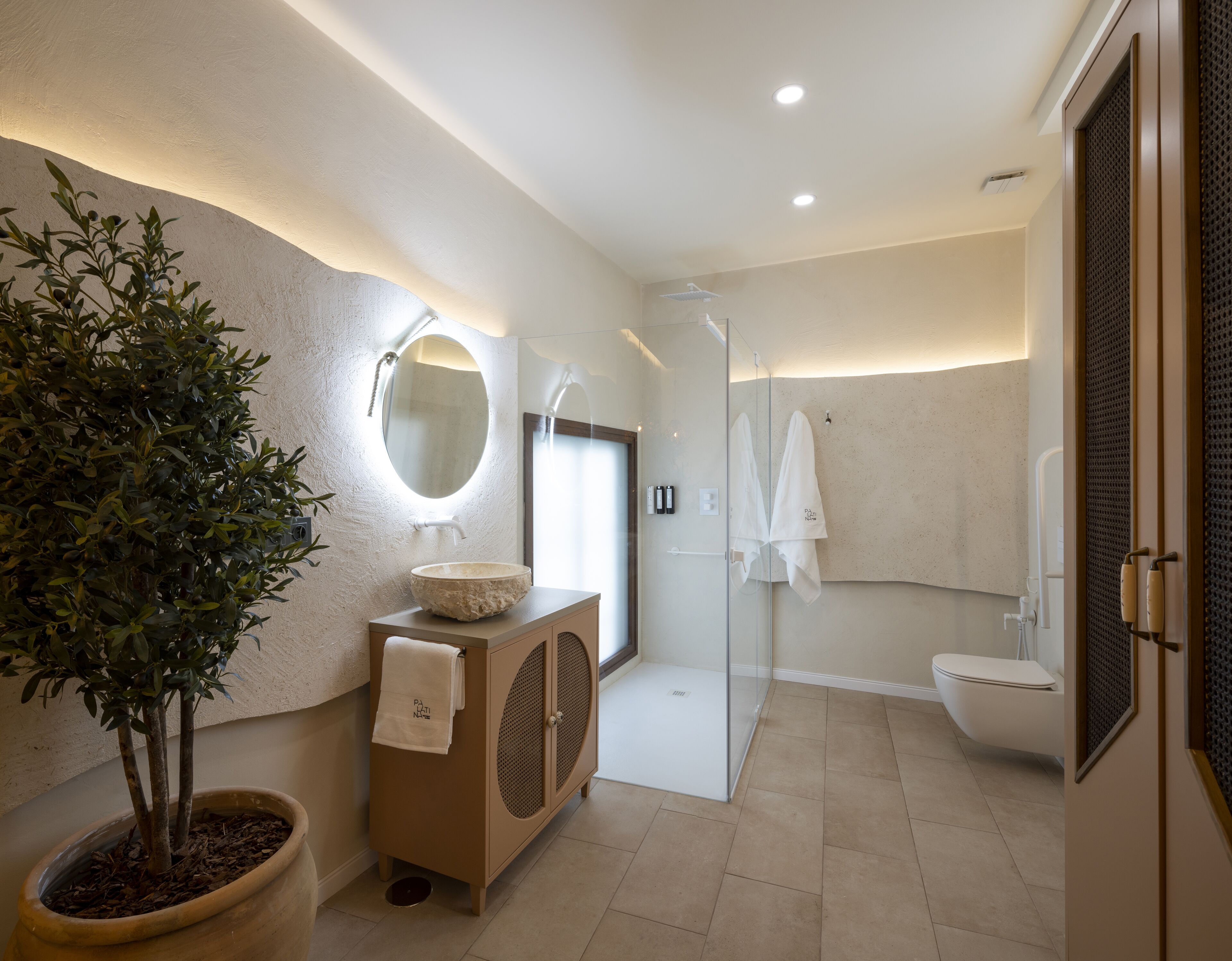 A modern bathroom with a large mirror, a sink, a shower, and a potted plant.
