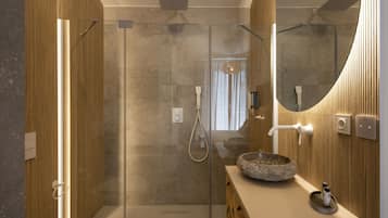 Un baño moderno con ducha envuelta en vidrio, tocador de madera con lavabo de piedra y un espejo grande.