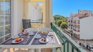 Un balcone con tavolo apparecchiato per la colazione, una sedia e vista su edifici e alberi.