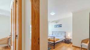 Una stanza arredata con un letto, un comodino, una poltrona in vimini e un condizionatore d'aria a muro.