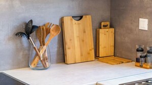 Una encimera de cocina con utensilios de madera dentro de un recipiente de vidrio, una tabla de cortar de madera y una especiero.